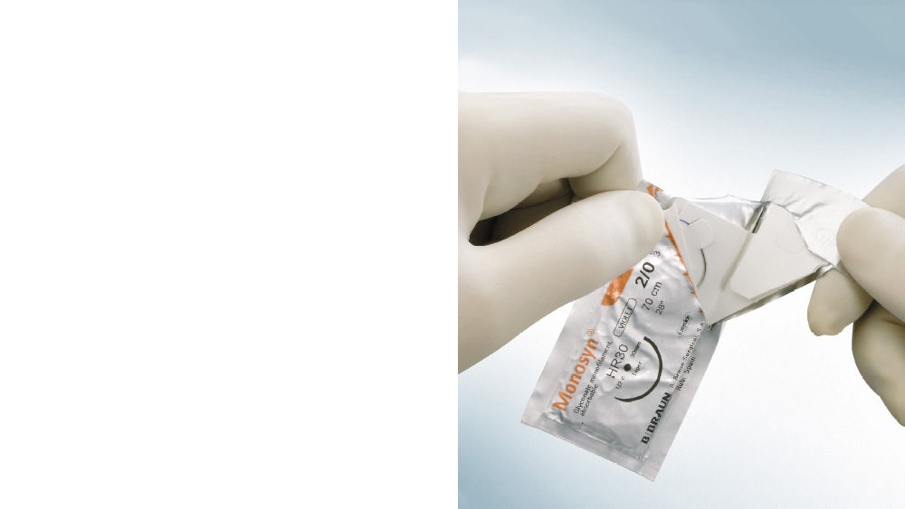 Gloved hands opening a Monosyn® suture package by peeling apart the sterile blister packaging, with the product label visible, shown against a light blue background
