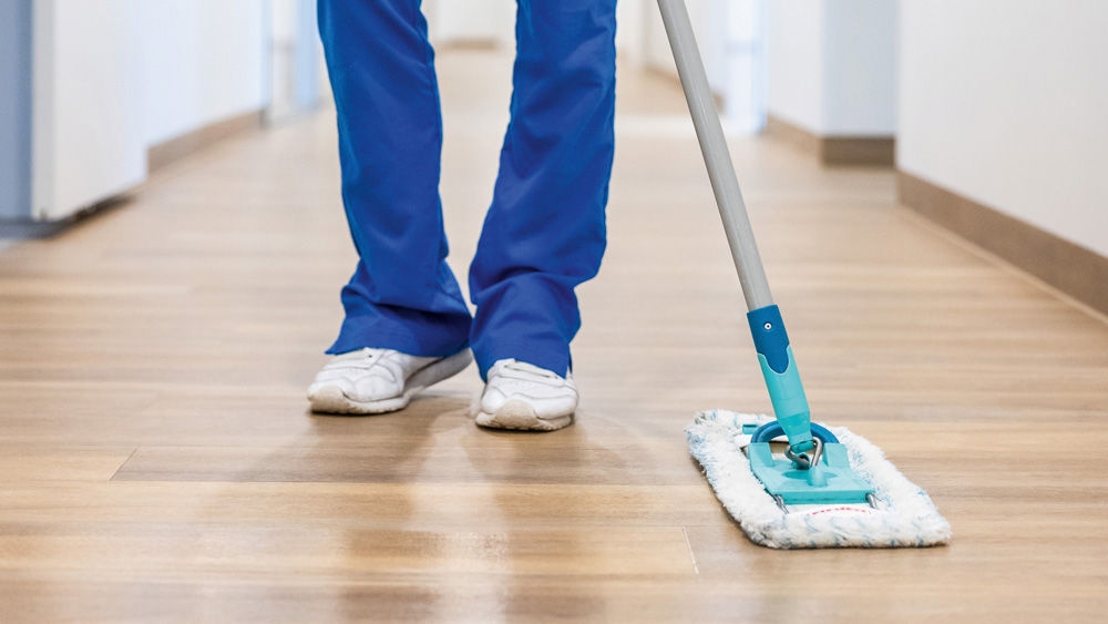 Veterinary nurse in medical scrubs mopping a clean corridor floor with a flat mop as part of routine cleaning and hygiene procedures in a healthcare or veterinary facility.