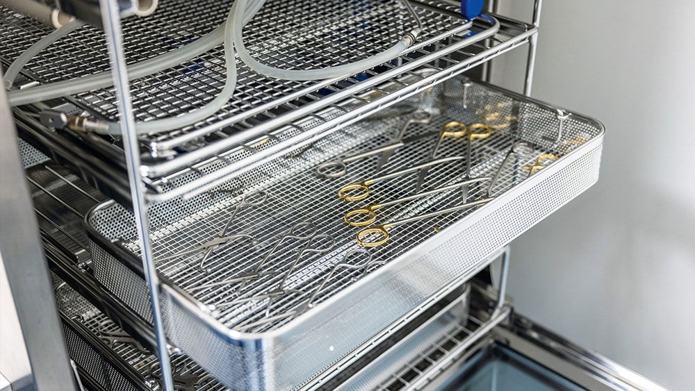 AESCULAP metal trays filled with surgical instruments placed inside a stainless steel sterilization unit.