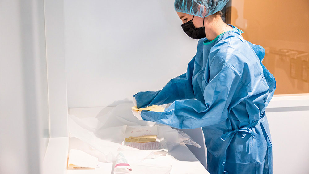 Veterinarian wearing a blue surgical gown, hair cover, and face mask, preparing surgical scrubs at a clean workstation.