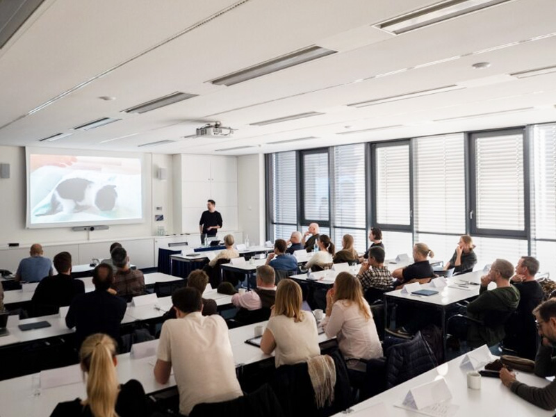 Group of people standing in front of a trade fair booth with a large veterinary-themed image in the background.
