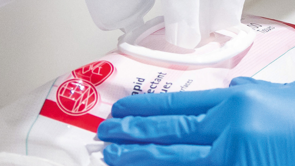 Gloved hands operating a dispenser to apply a medical disinfectant.