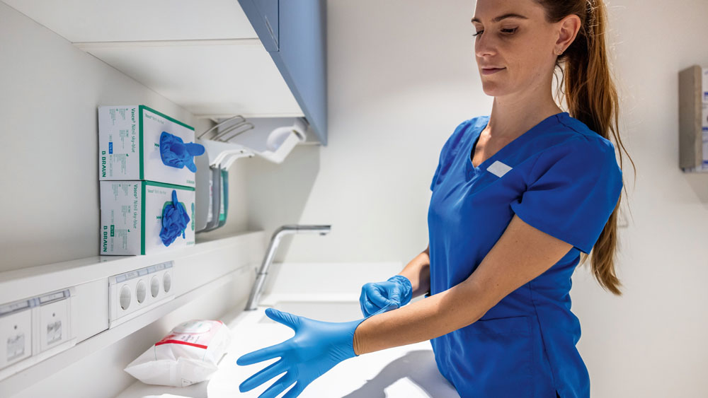 A veterinary professional in a clinical workspace putting on disposable gloves next to organized medical supplies.