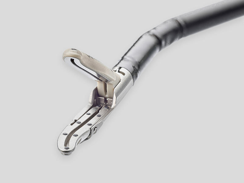 Close-up of the Caiman® surgical instrument showing its Seal & Cut vessel-sealing jaw at the tip, displayed against a light background with product branding on the left.